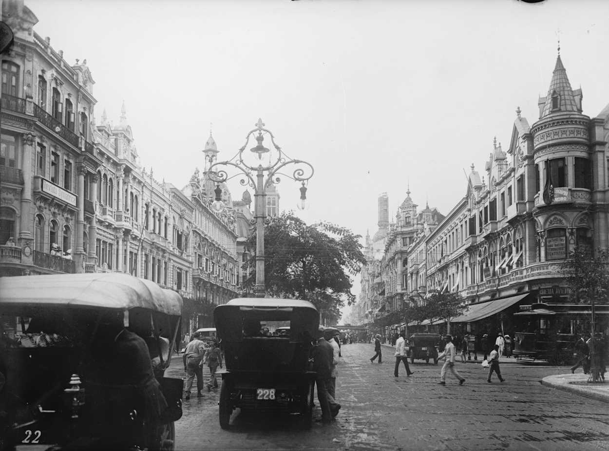 Historic Avenida Rio Branco in Rio de Janeiro, Brazil (Early 1900s) Vintage black and white photo of Avenida Rio Branco in Rio de Janeiro, featuring early 20th-century cars, architecture, and pedestrians.